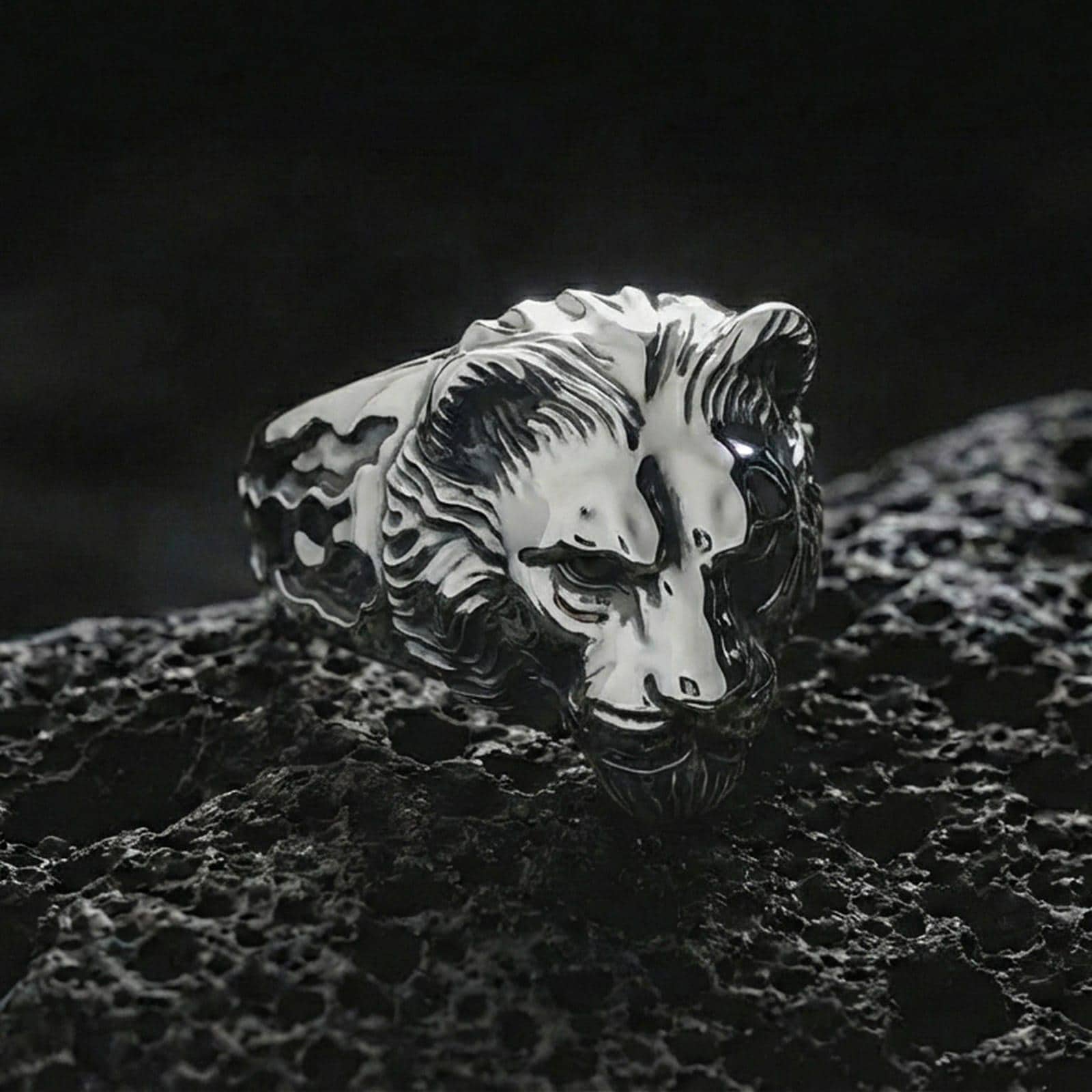 Polished silver lioness ring displayed on textured volcanic rock with sharp macro detail and soft shadows