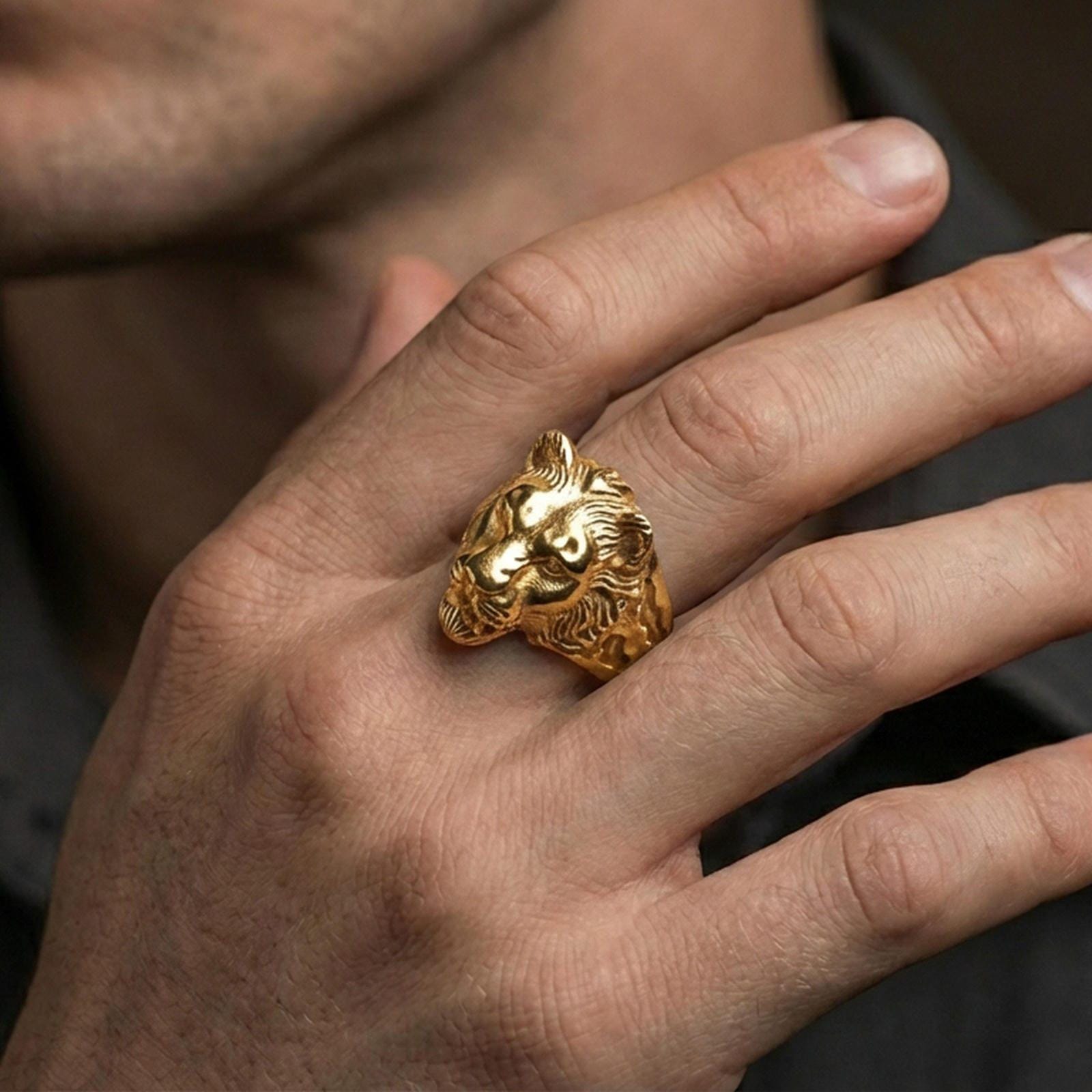 Gold plated lioness ring worn on a finger with dark minimal background, focusing on the powerful feline profile