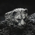 Load image into Gallery viewer, Close-up of an oxidized sterling silver lioness head ring on porous volcanic rock in a dark studio scene
