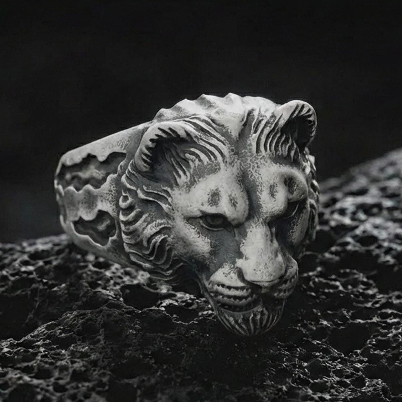 Close-up of an oxidized sterling silver lioness head ring on porous volcanic rock in a dark studio scene