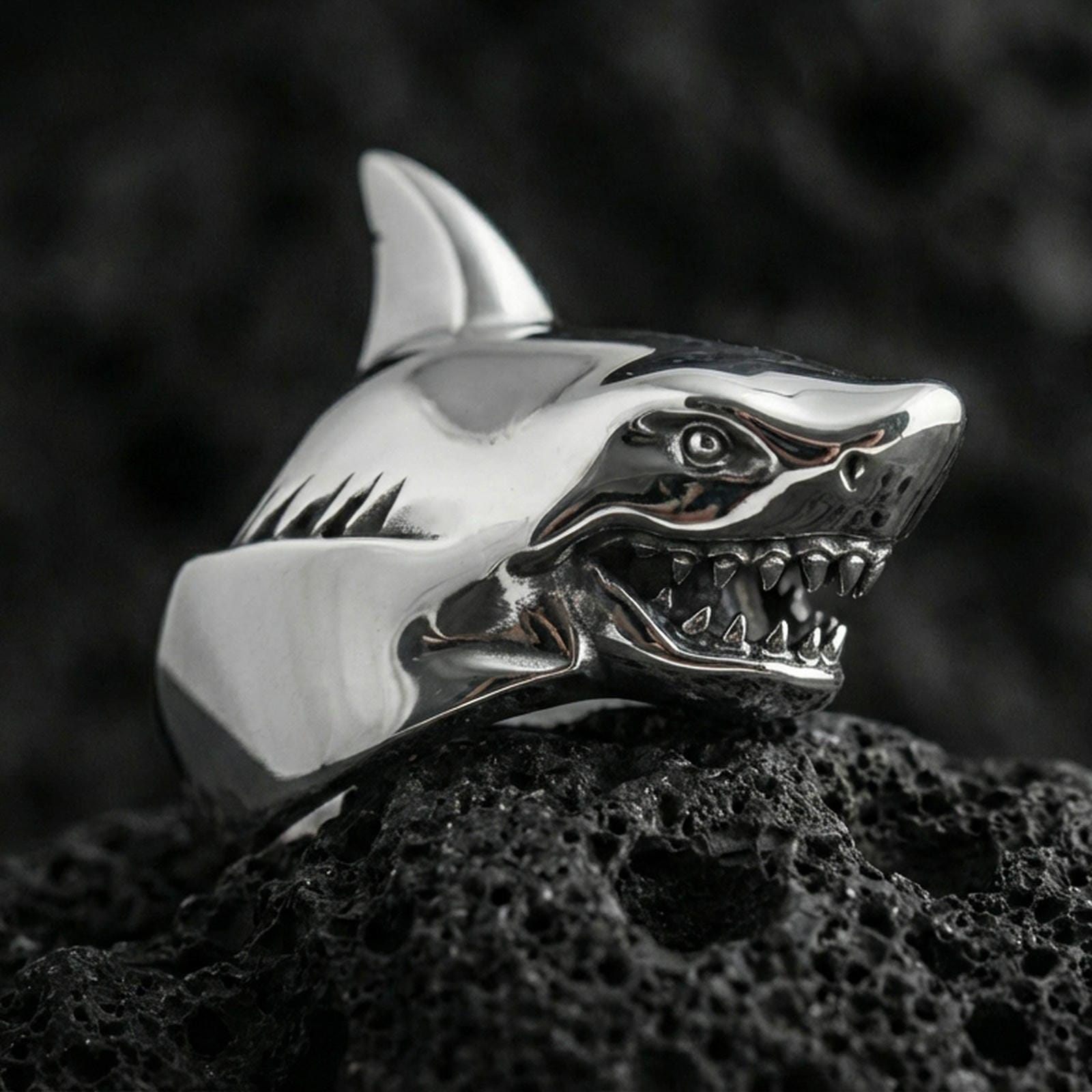 Polished silver shark ring on textured volcanic stone with macro focus on the jawline and teeth detailing