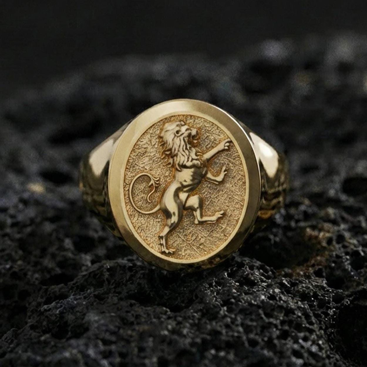 Gold plated heraldic lion signet ring on volcanic rock in a dark studio setting, detailed macro shot emphasizing the raised lion figure and premium shine