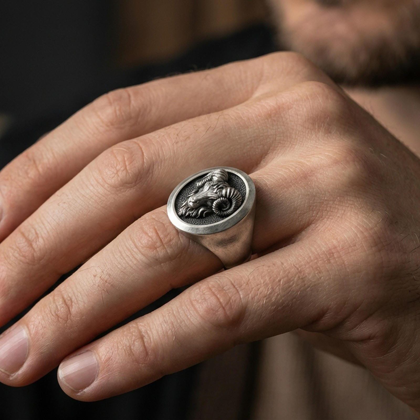 Oxidized sterling silver ram ring worn on a finger, side angle showing the raised oval face and horn detail