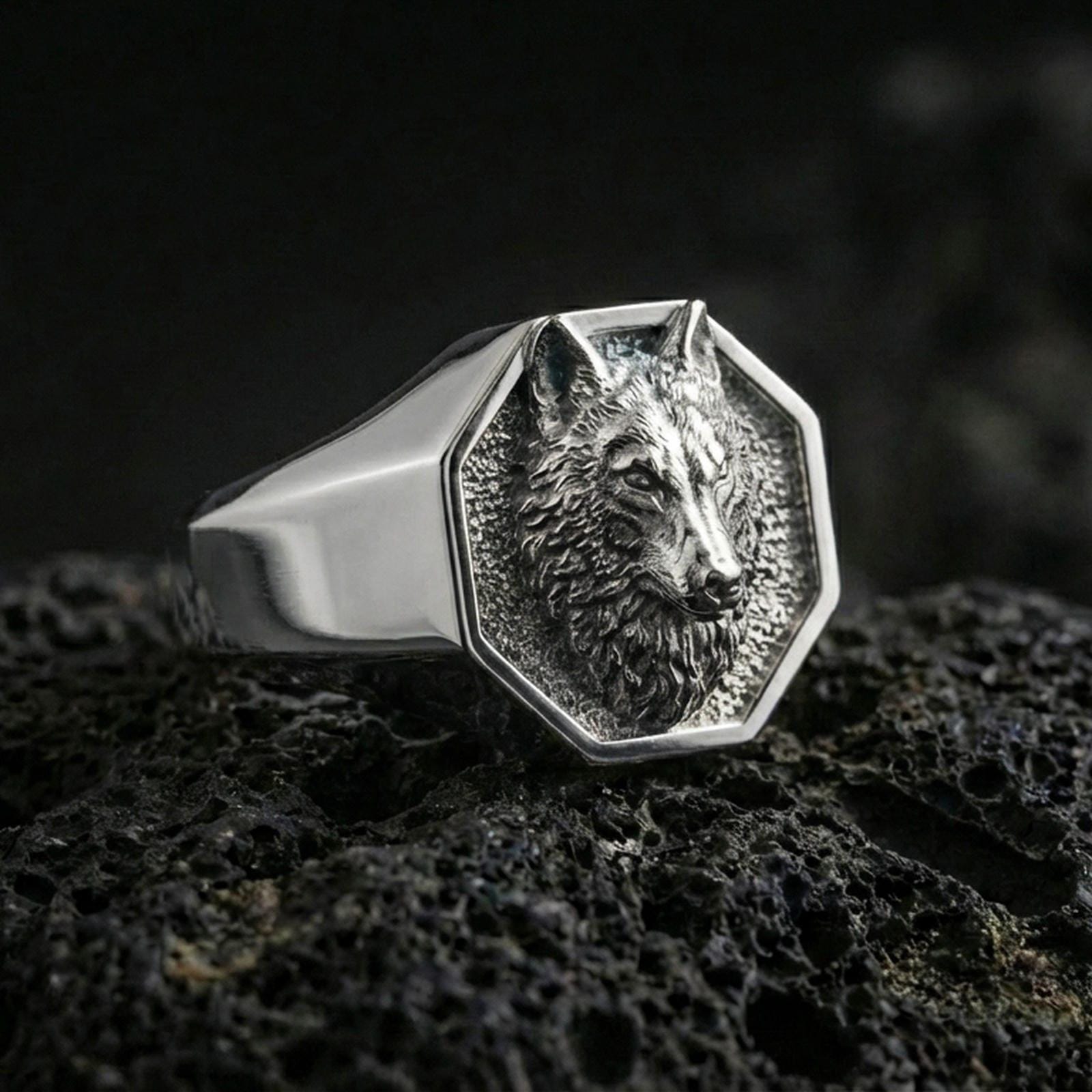 Polished silver geometric wolf ring on textured volcanic stone, macro focus on the wolf head relief and edges