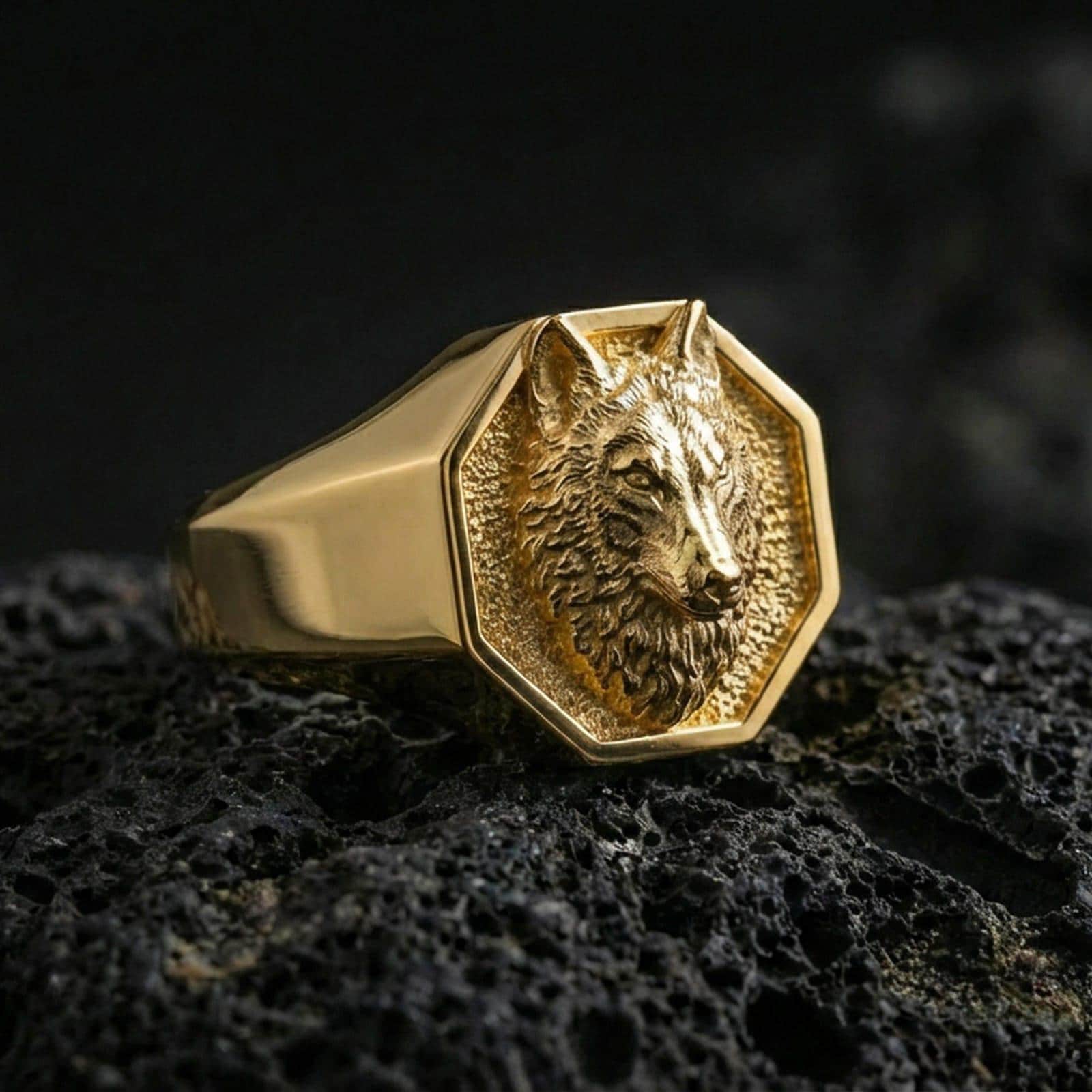 Gold plated octagon wolf signet ring on black volcanic rock, close-up emphasizing the sculpted fur texture