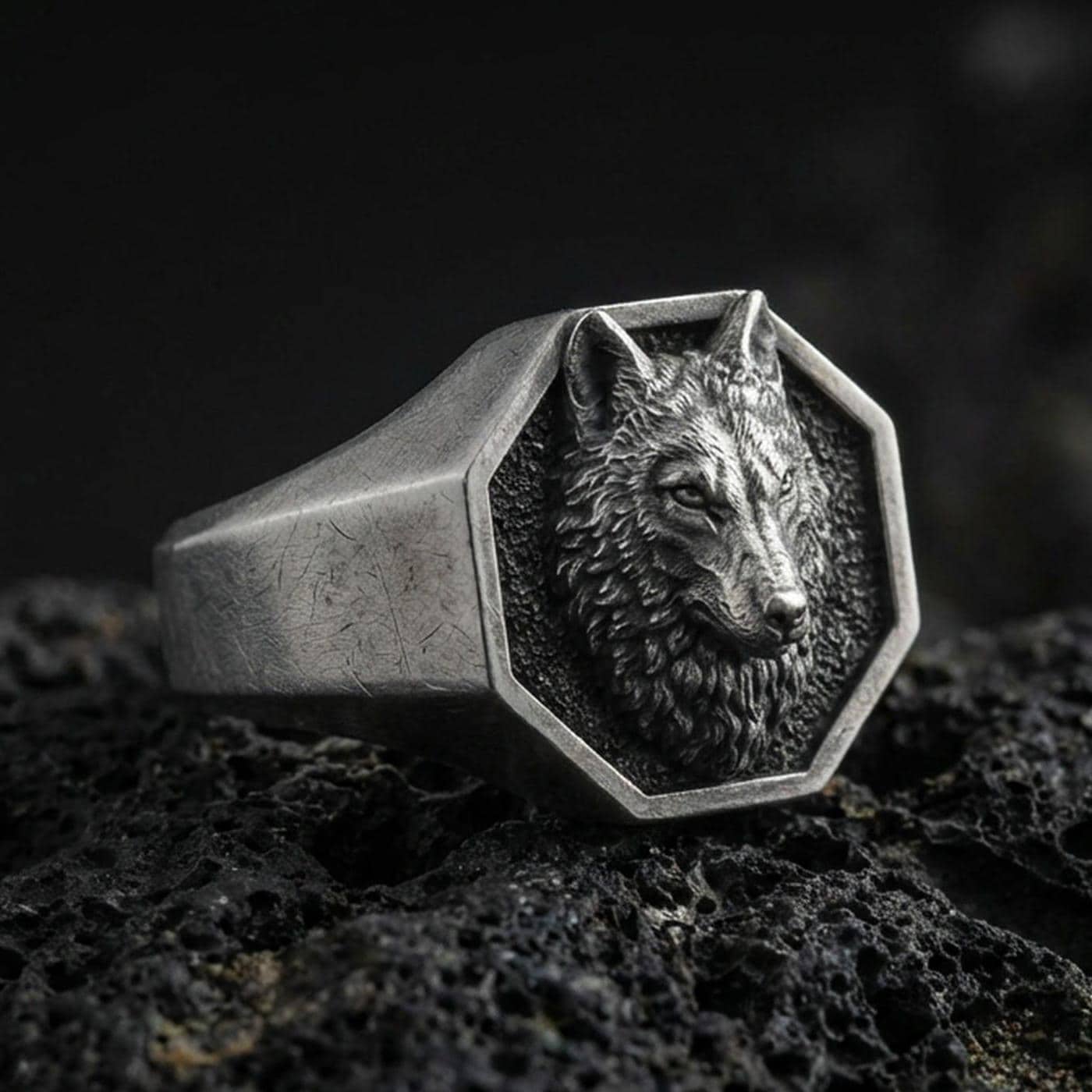 Close-up of an oxidized sterling silver octagon wolf signet ring on porous volcanic rock with dark studio lighting
