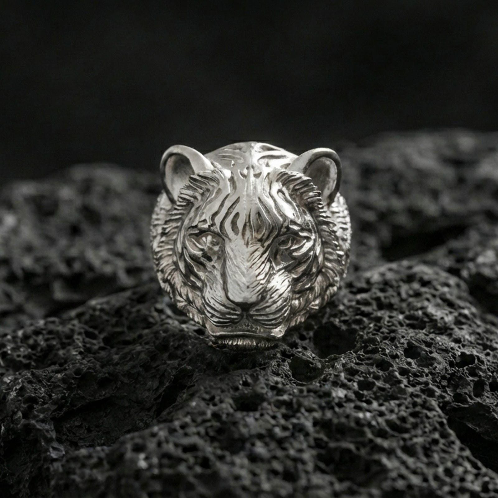 Polished silver tiger face ring on textured volcanic stone, macro focus on the tribal stripe engraving