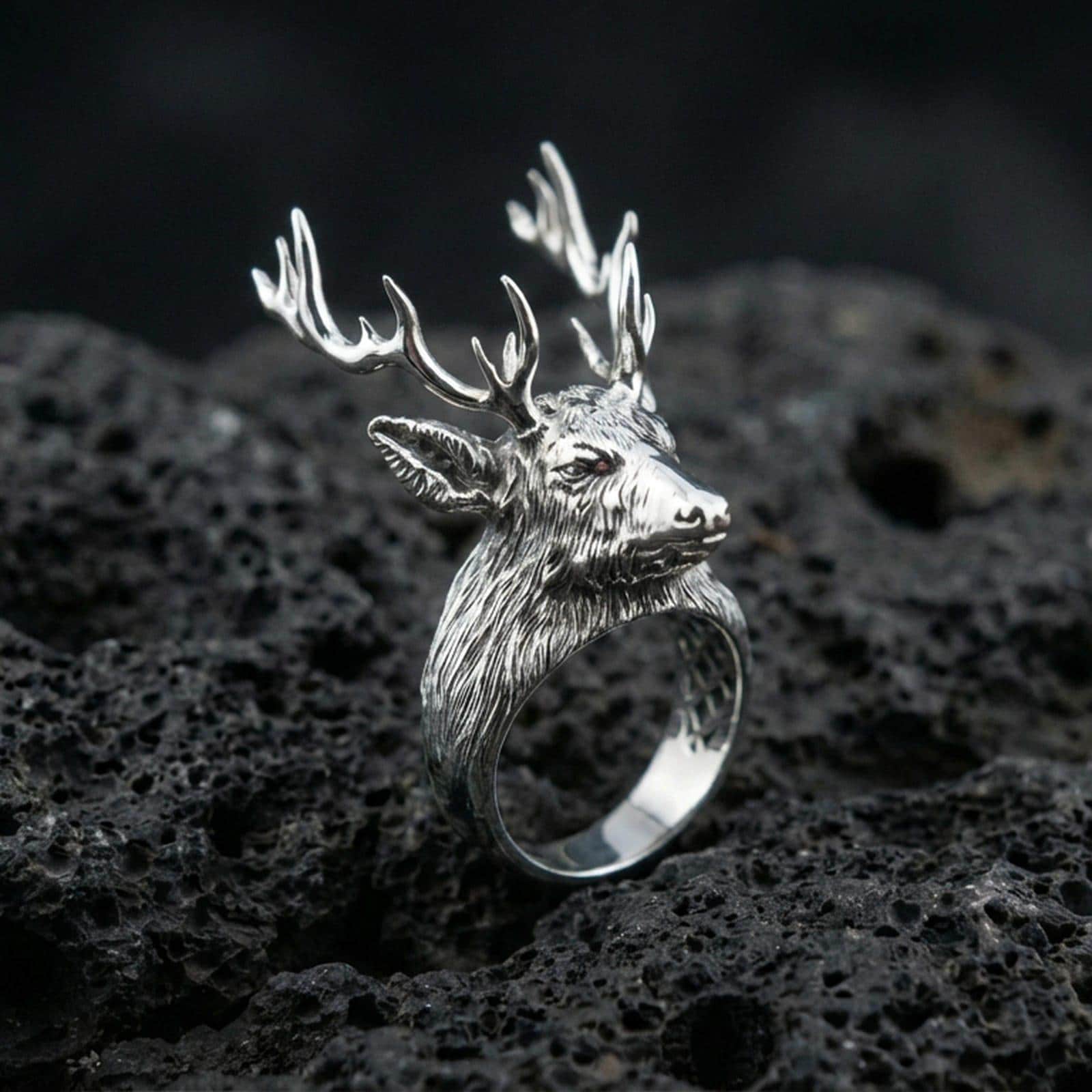 Polished silver deer antler ring on textured volcanic stone, macro focus on the carved fur and antlers