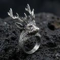 Load image into Gallery viewer, Close-up of an oxidized sterling silver stag head ring on porous volcanic rock with dramatic studio lighting
