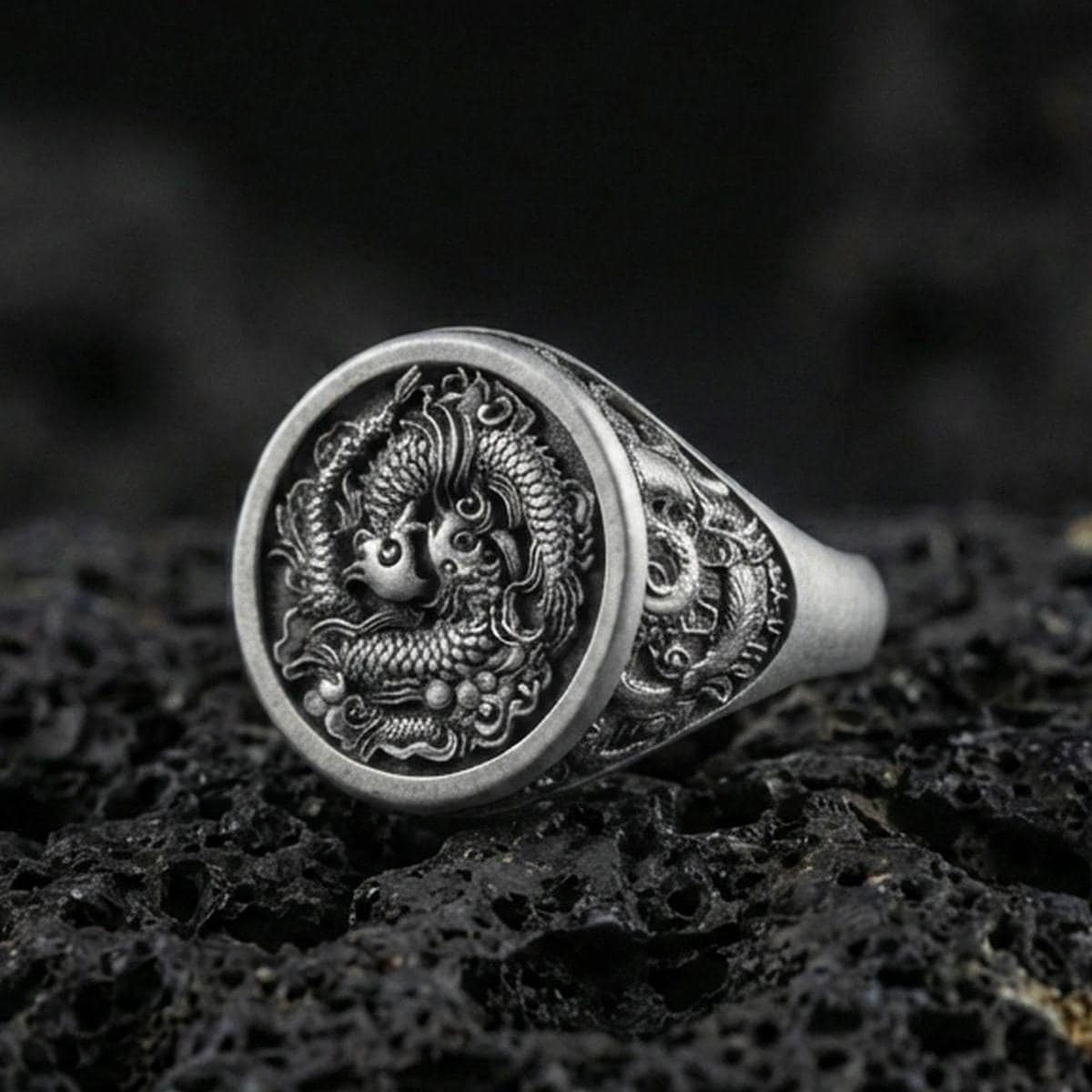 Close-up of an oxidized sterling silver yin yang koi fish signet ring on porous volcanic rock in a dark studio