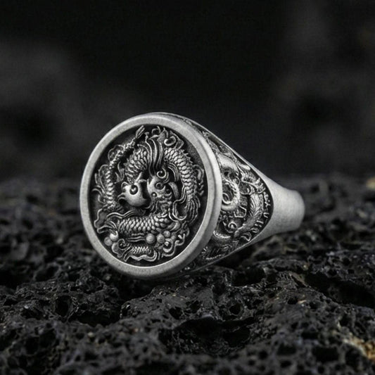 Close-up of an oxidized sterling silver yin yang koi fish signet ring on porous volcanic rock in a dark studio