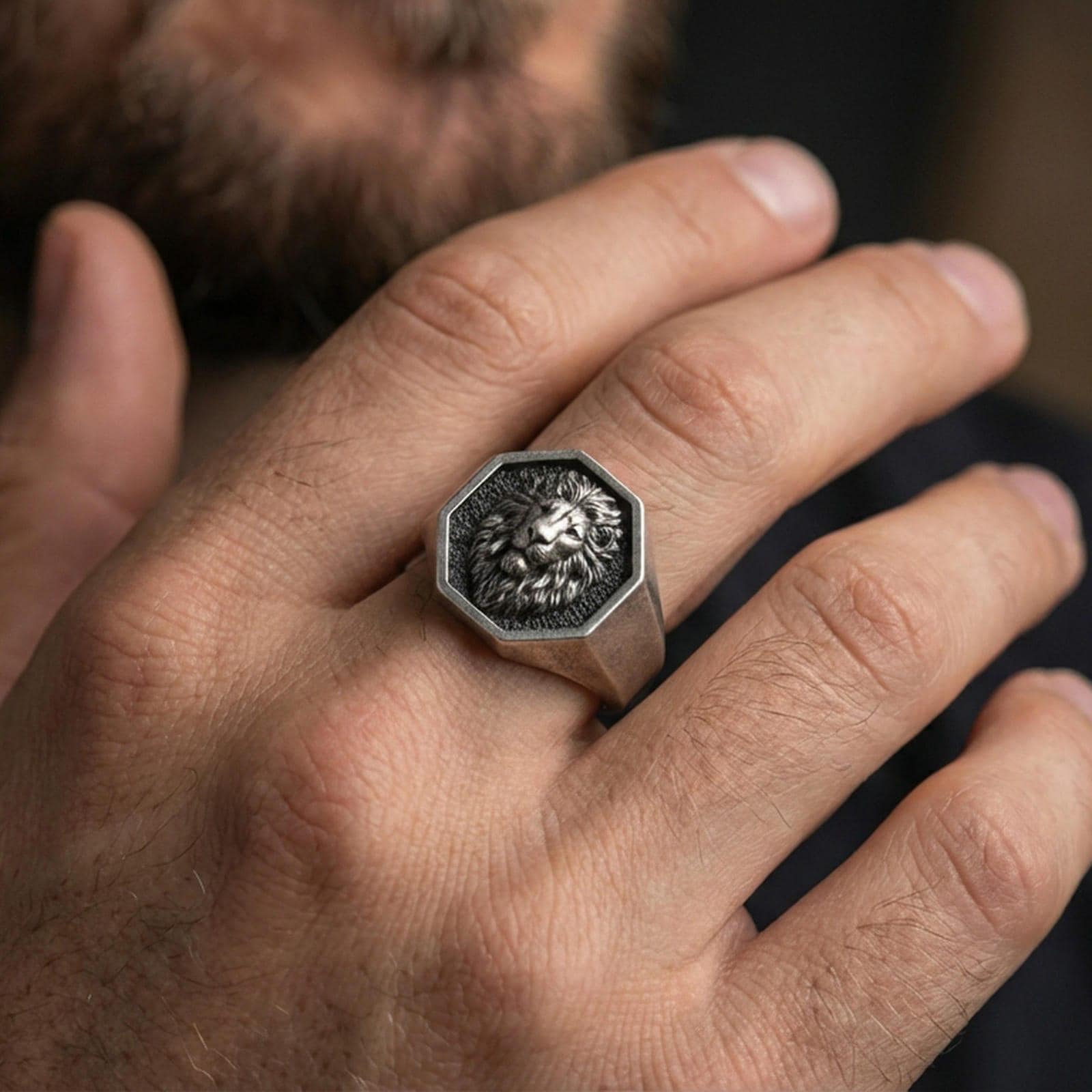 Oxidized sterling silver lion signet ring worn on a finger, front view showing the octagon face and lion portrait