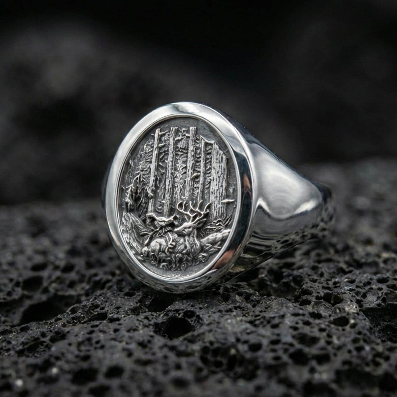 Polished silver nature signet ring on textured volcanic stone, macro focus on the woodland engraving