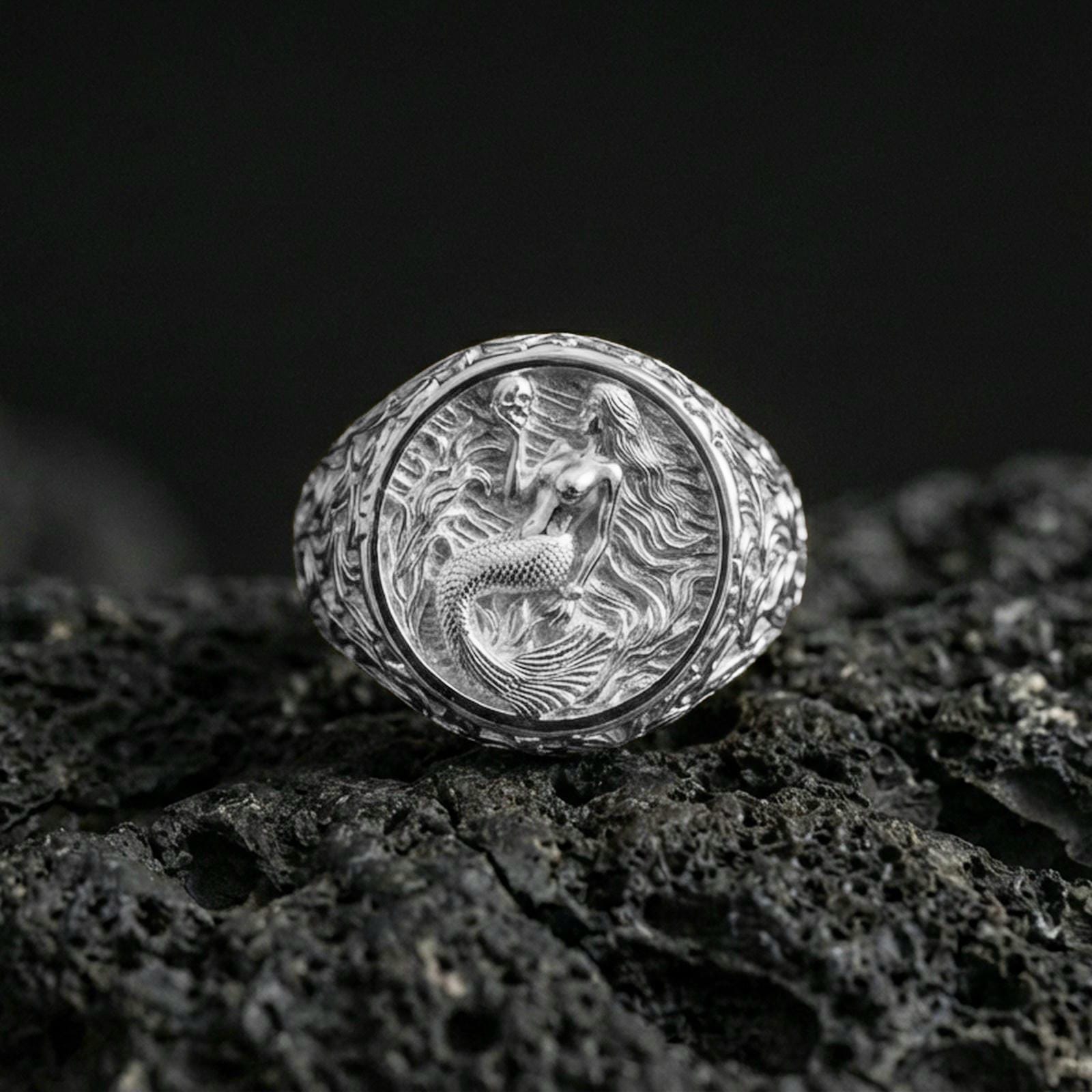Polished silver mermaid signet ring on black volcanic stone, detailed mermaid relief and wave background, premium studio product photo