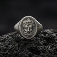 Load image into Gallery viewer, Oxidized Poseidon ring on volcanic rock, Greek god king portrait signet, textured background, macro studio jewelry photo
