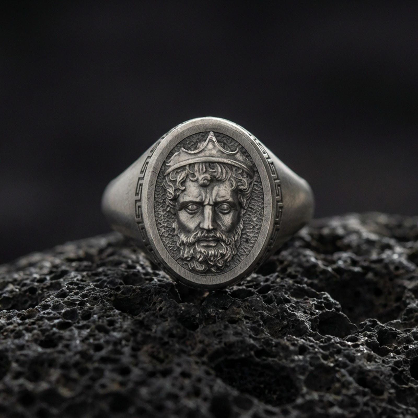 Oxidized Poseidon ring on volcanic rock, Greek god king portrait signet, textured background, macro studio jewelry photo