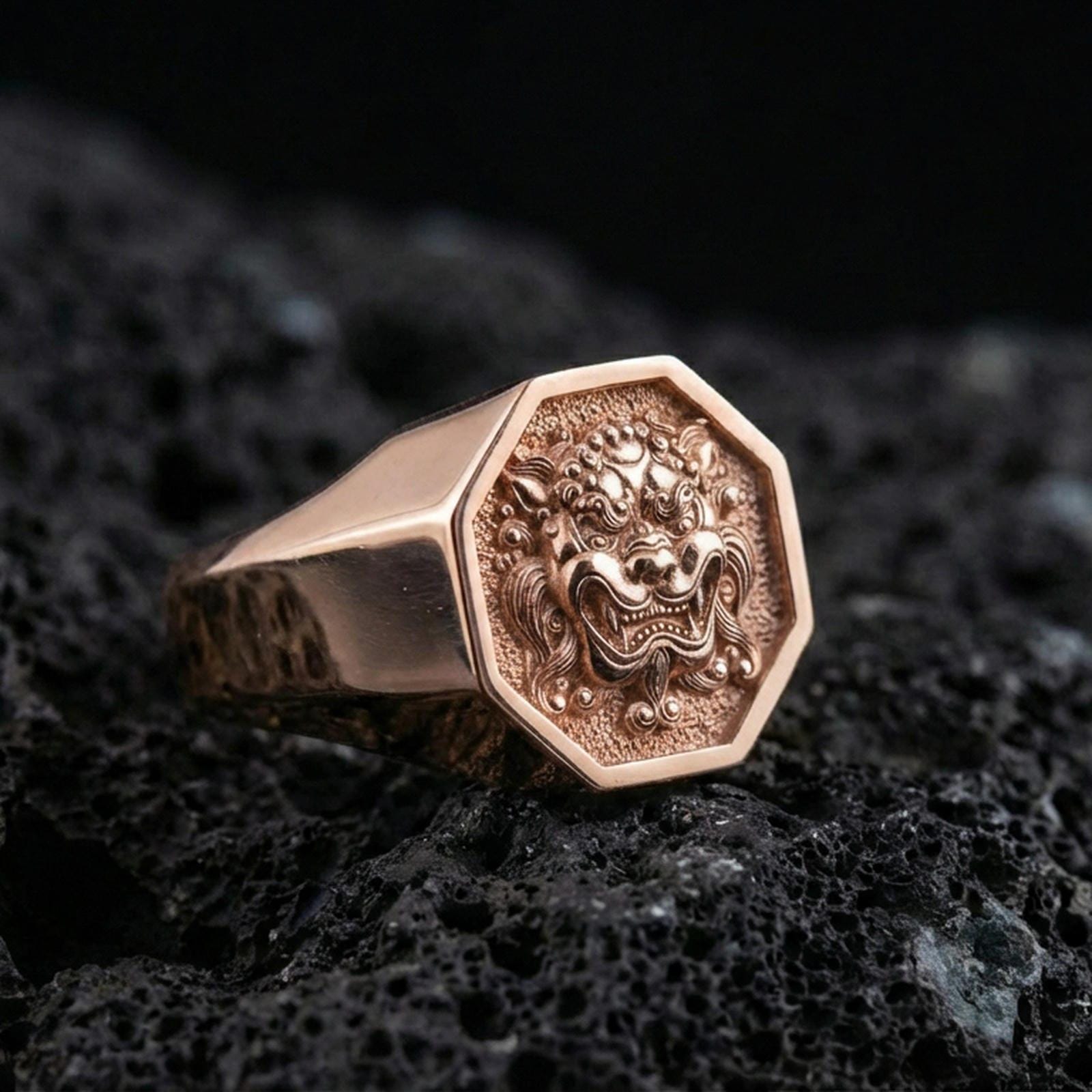 Octagon rose gold plated Foo Dog signet ring on volcanic rock, ornate guardian lion face relief, luxury studio close-up
