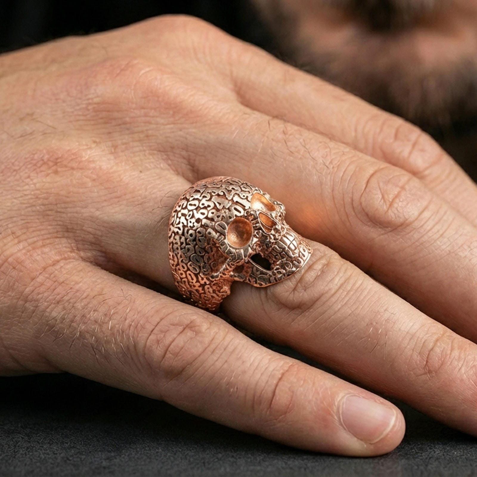 Cronus skull ring in a rose gold plated finish on finger, detailed numerology pattern across the skull, lifestyle wear photo