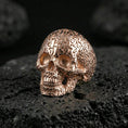 Load image into Gallery viewer, Cronus skull numerology ring in a rose gold plated finish on volcanic rock, ornate number-covered skull detail, luxury studio close-up
