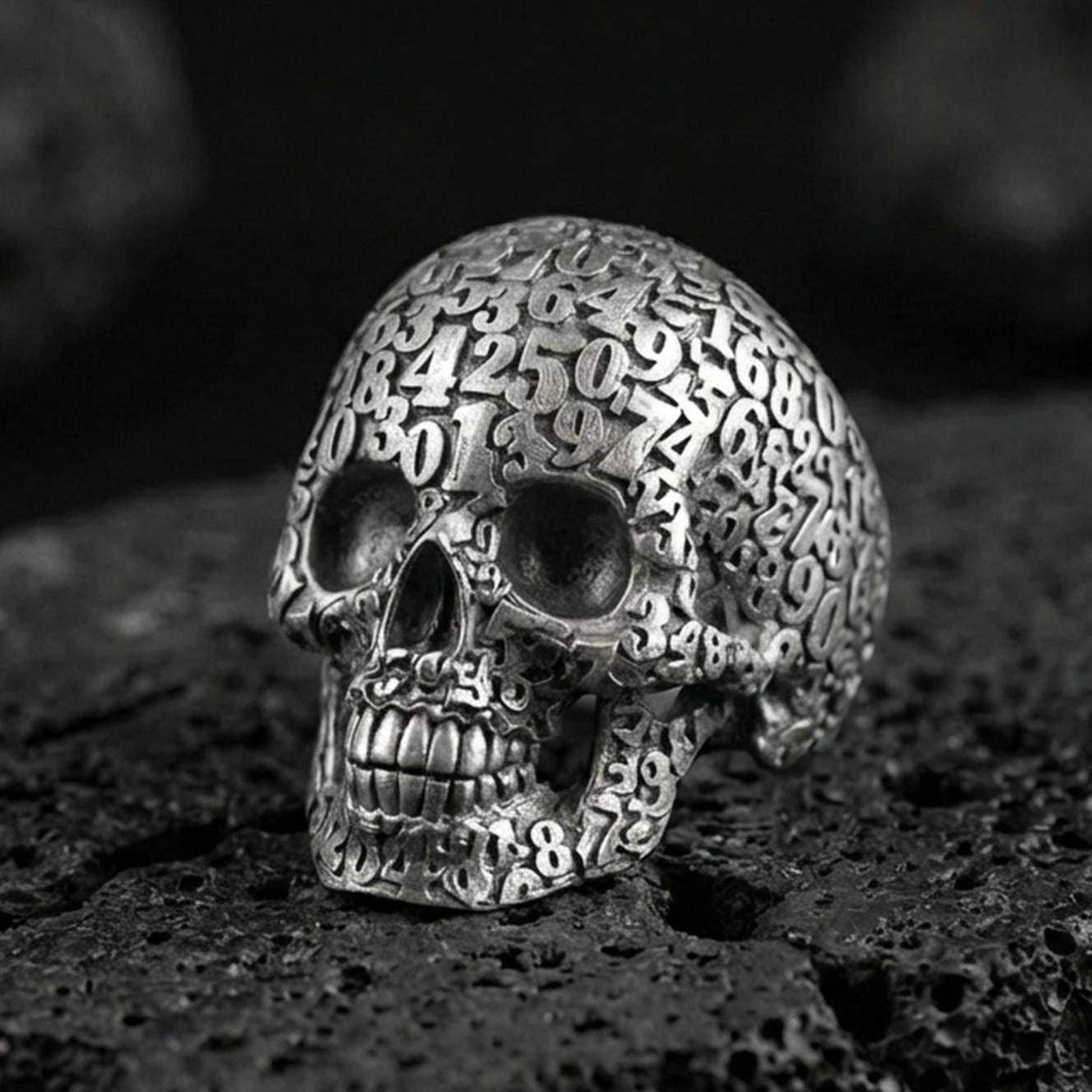 925 sterling silver numerology skull signet ring in an oxidized finish on volcanic rock, Cronus-inspired memento mori design, macro studio shot