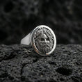 Load image into Gallery viewer, Oval sterling silver Odin signet ring in polished silver finish on volcanic rock, Viking deity face relief with braided border, close-up photo
