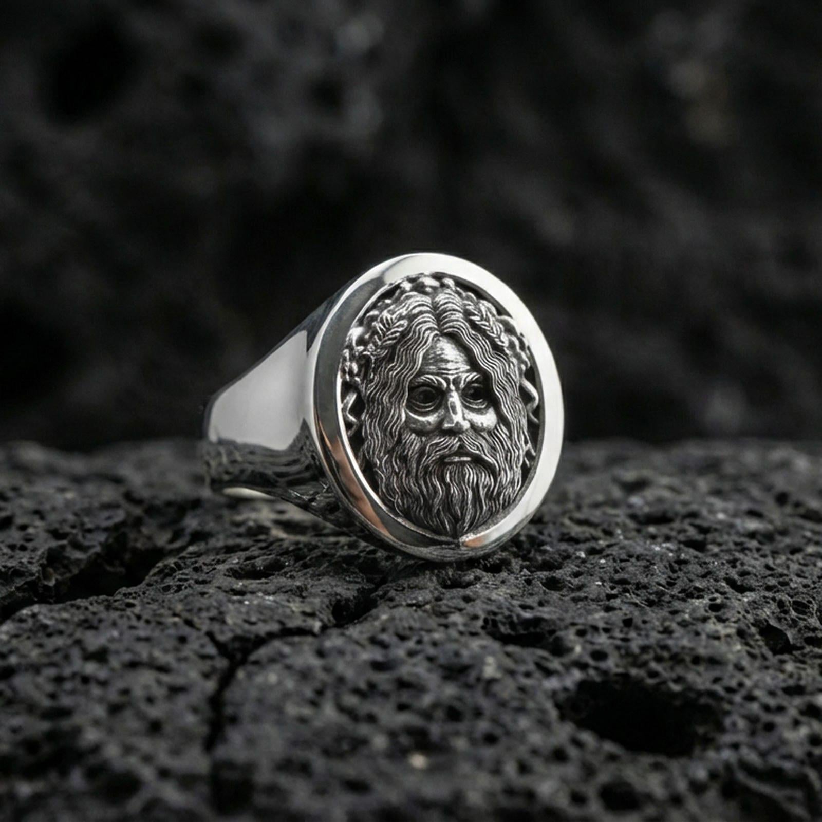Oval sterling silver Odin signet ring in polished silver finish on volcanic rock, Viking deity face relief with braided border, close-up photo