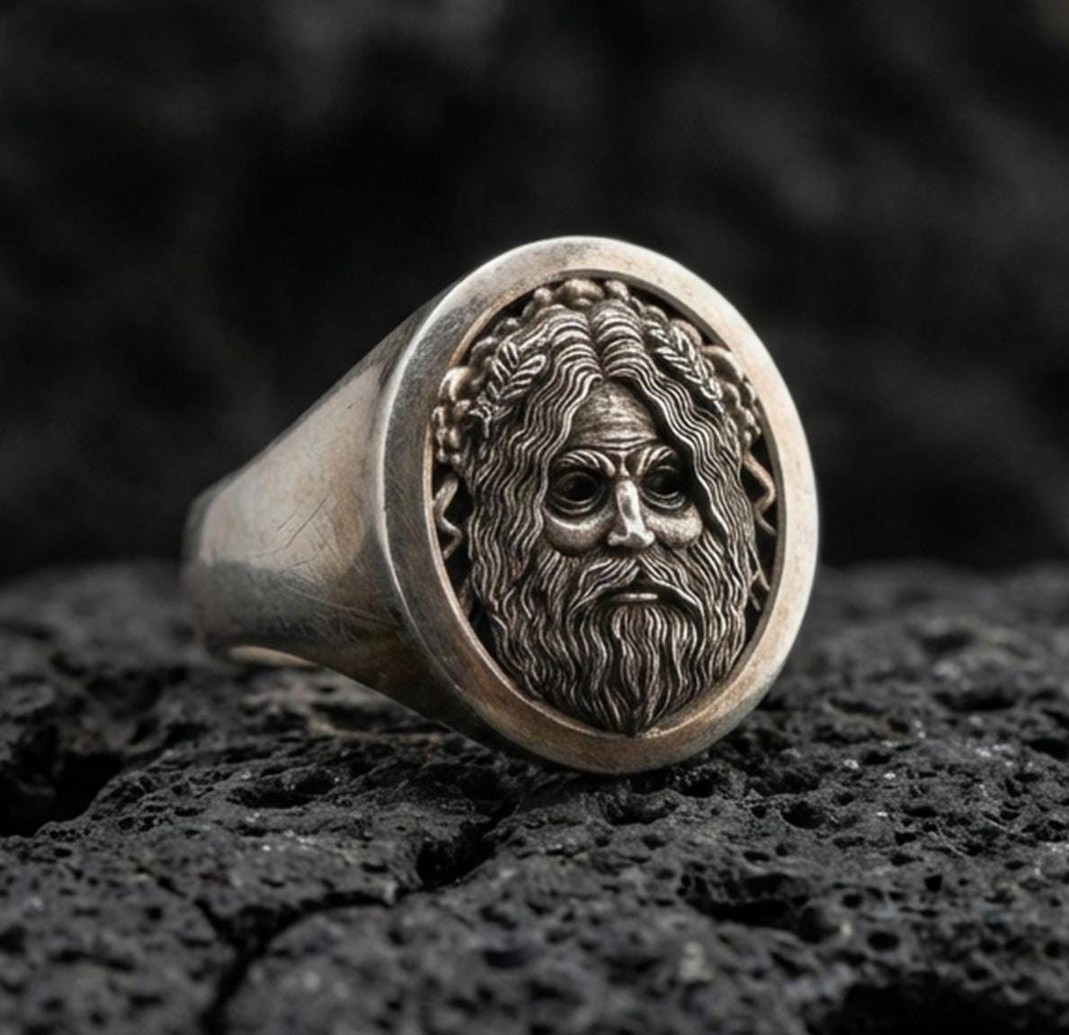 Oval Odin Norse god signet ring in an oxidized sterling silver finish on volcanic rock, detailed bearded portrait engraving, macro studio product shot