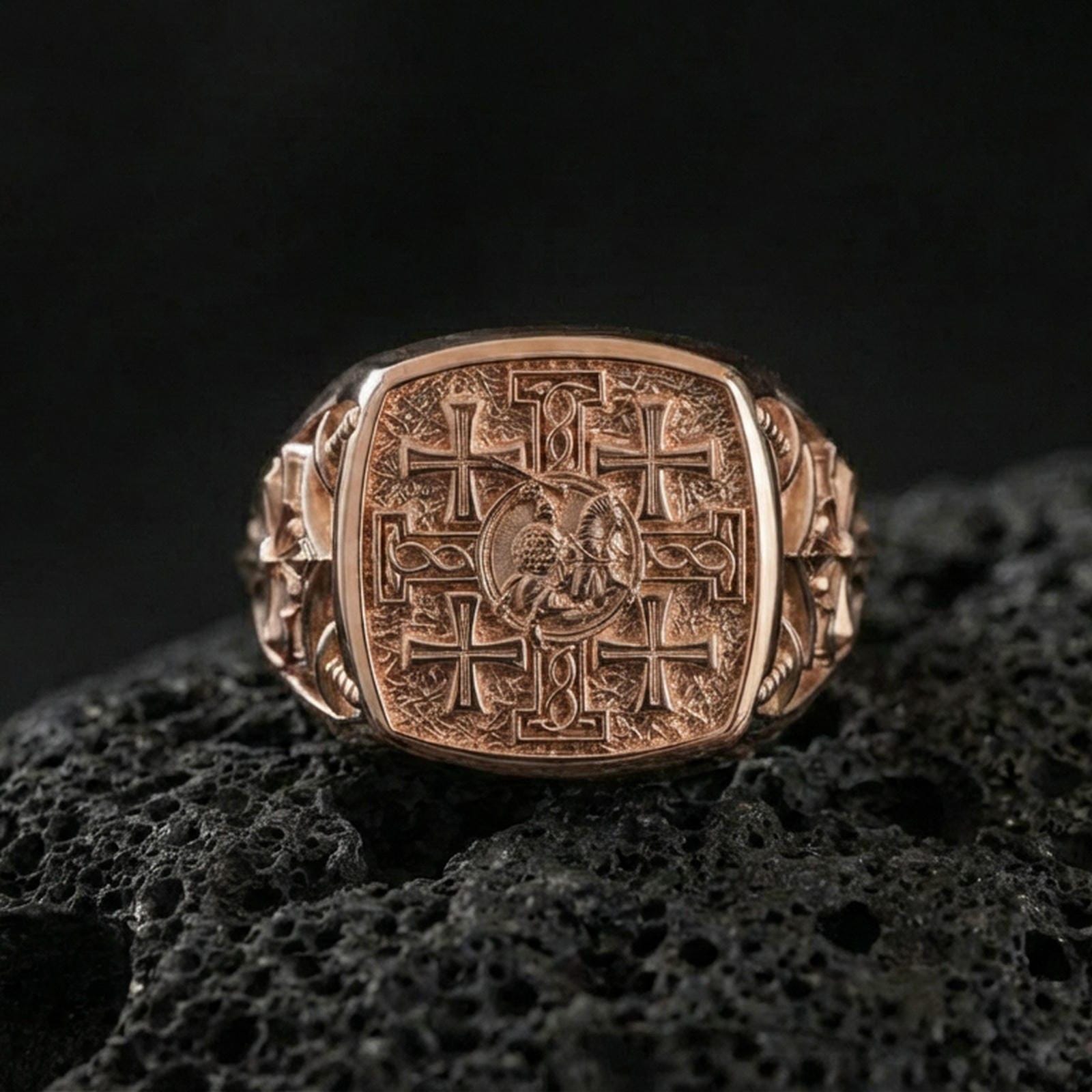 Jerusalem Cross signet ring in a rose gold plated finish on volcanic rock, medieval cross design with textured background, luxury studio close-up