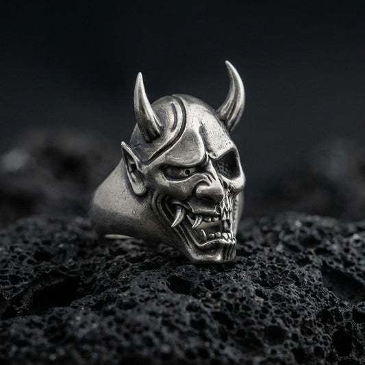 Sterling silver undead oni mask ring in an oxidized finish on volcanic rock, Japanese yokai demon face with horns, macro studio product shot