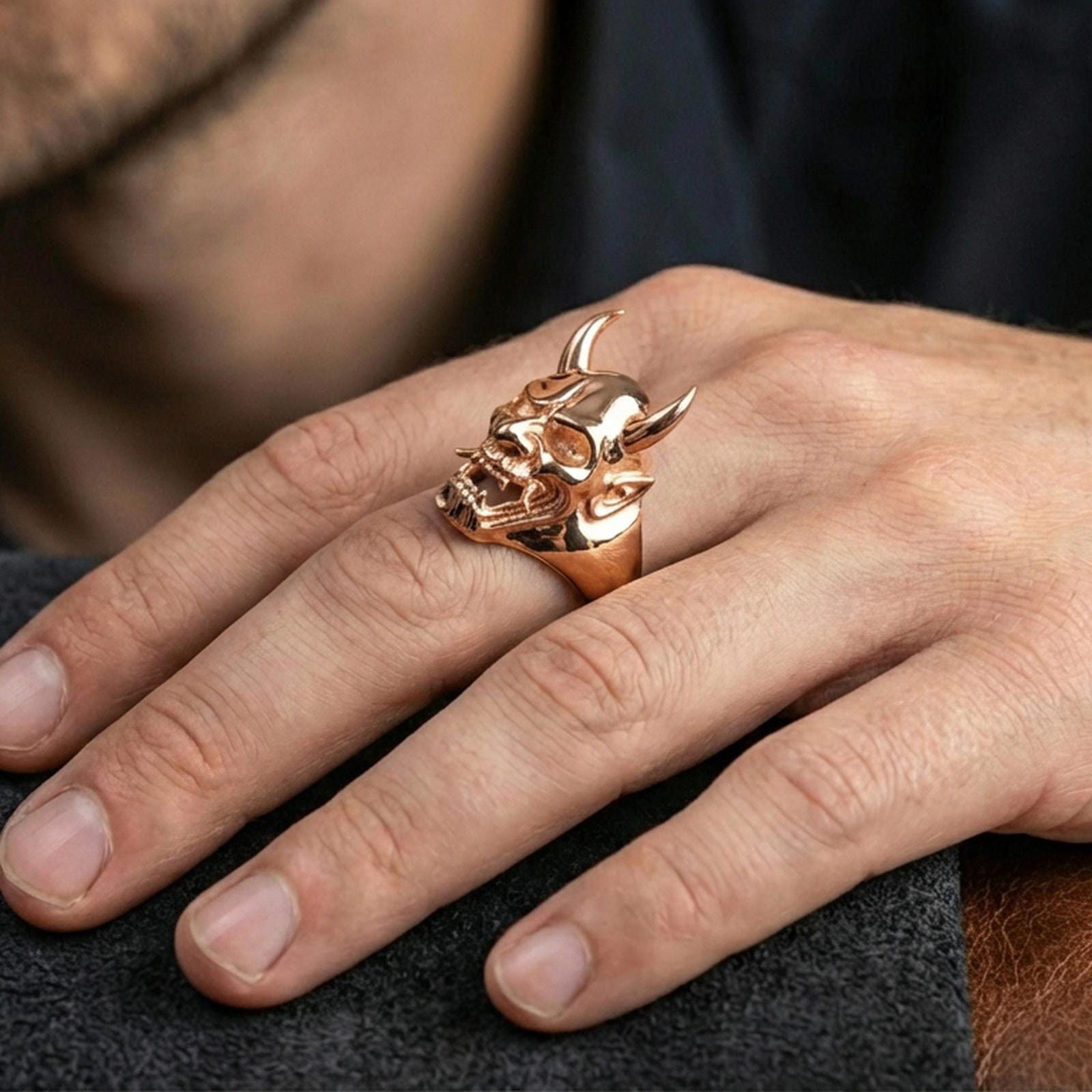 Oni skull ring in a rose gold plated finish on finger, detailed horned yokai mask profile, lifestyle wear photo