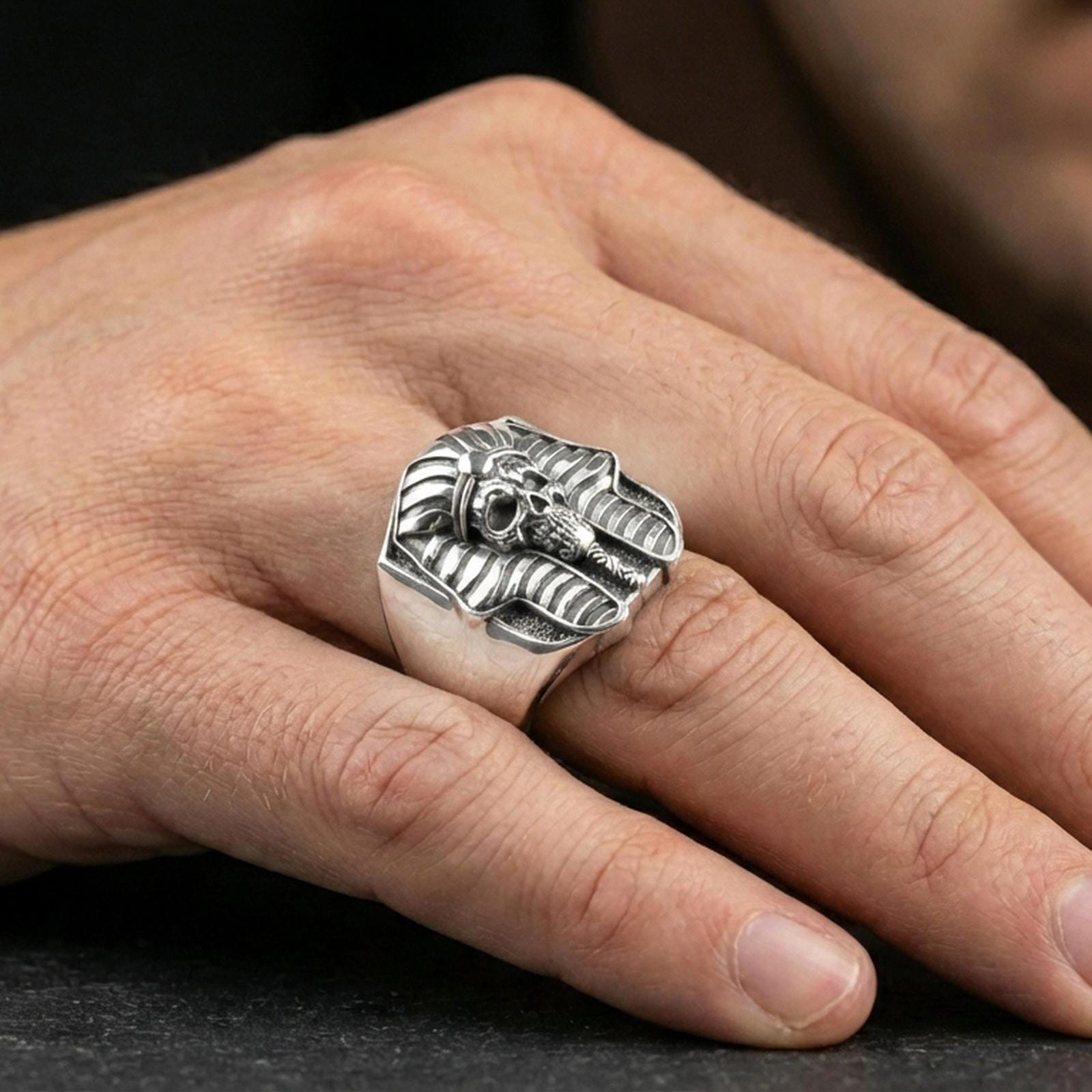 Pharaoh skull ring in polished silver finish on finger, ancient Egypt headdress carving and skull face detail, natural lifestyle wear shot