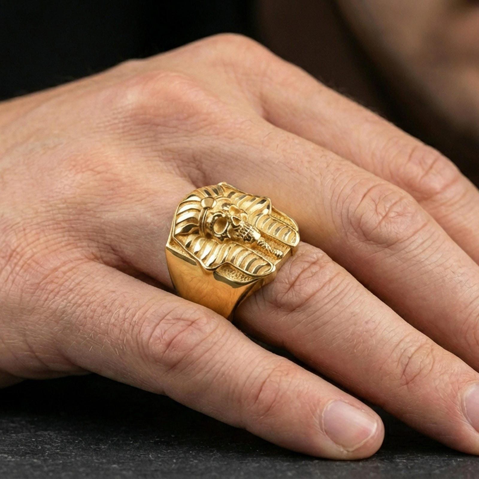 Pharaoh skull ring in a gold plated finish worn on finger, bold Egyptian memento mori statement ring, masculine lifestyle close-up