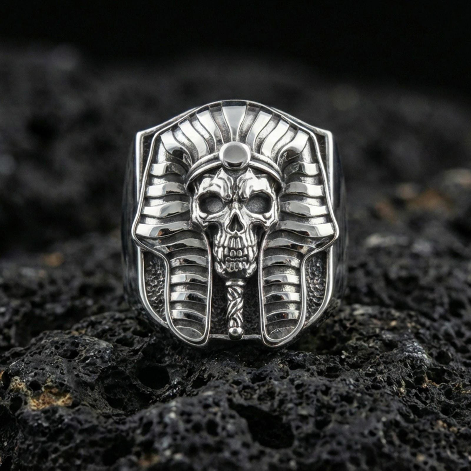 Sterling silver pharaoh skull ring in polished silver finish on volcanic rock, detailed Egyptian headdress and skull carving, close-up photo