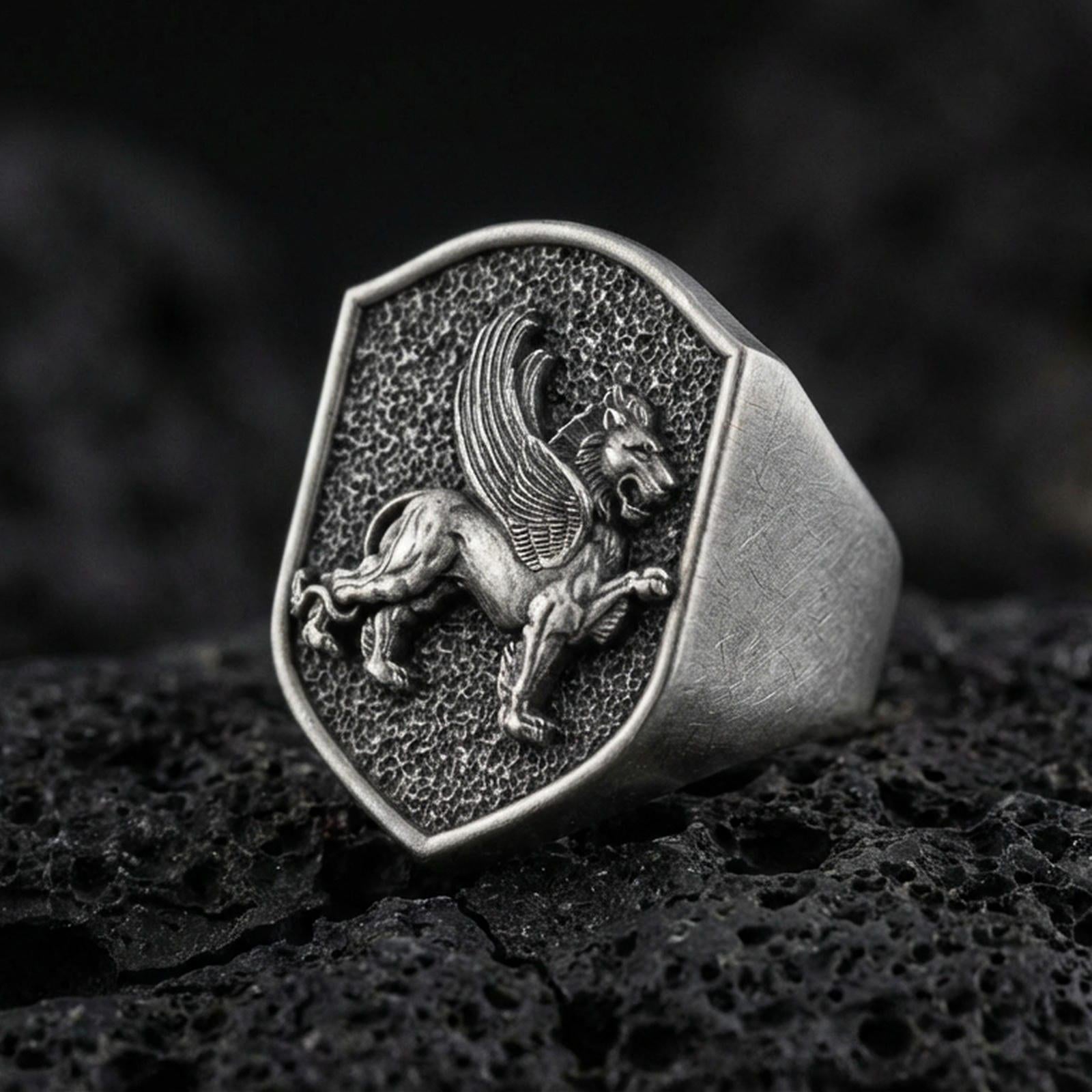 Sterling silver gryphon signet ring in an oxidized finish on volcanic rock, mythical griffin relief on shield-shaped face, macro studio product shot