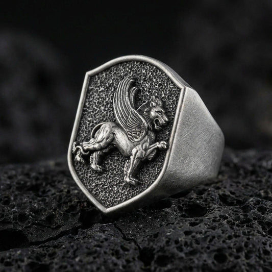 Sterling silver gryphon signet ring in an oxidized finish on volcanic rock, mythical griffin relief on shield-shaped face, macro studio product shot