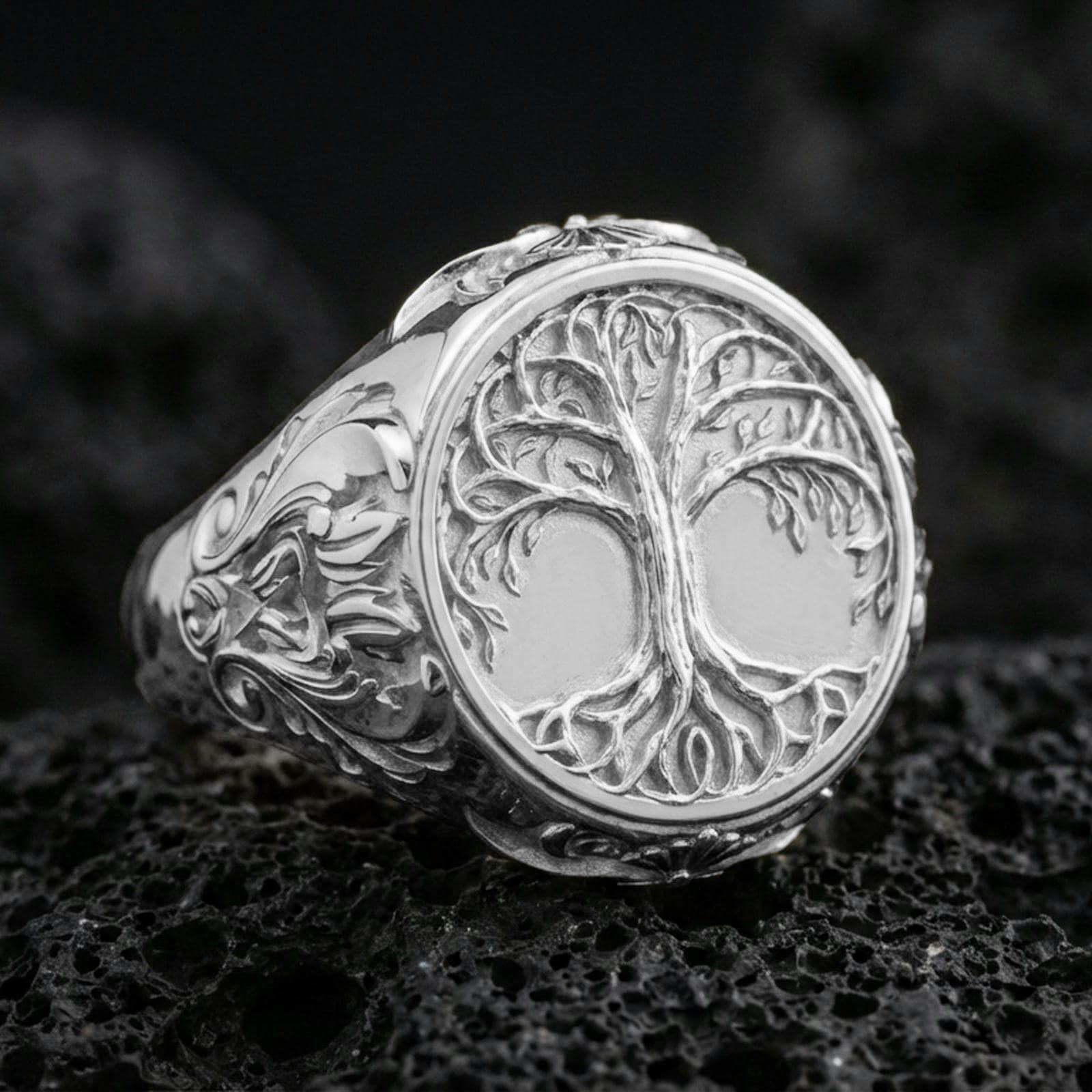 Yggdrasil ring in polished silver finish on volcanic rock, detailed tree of life engraving with ornamental side scrollwork, premium close-up product photo