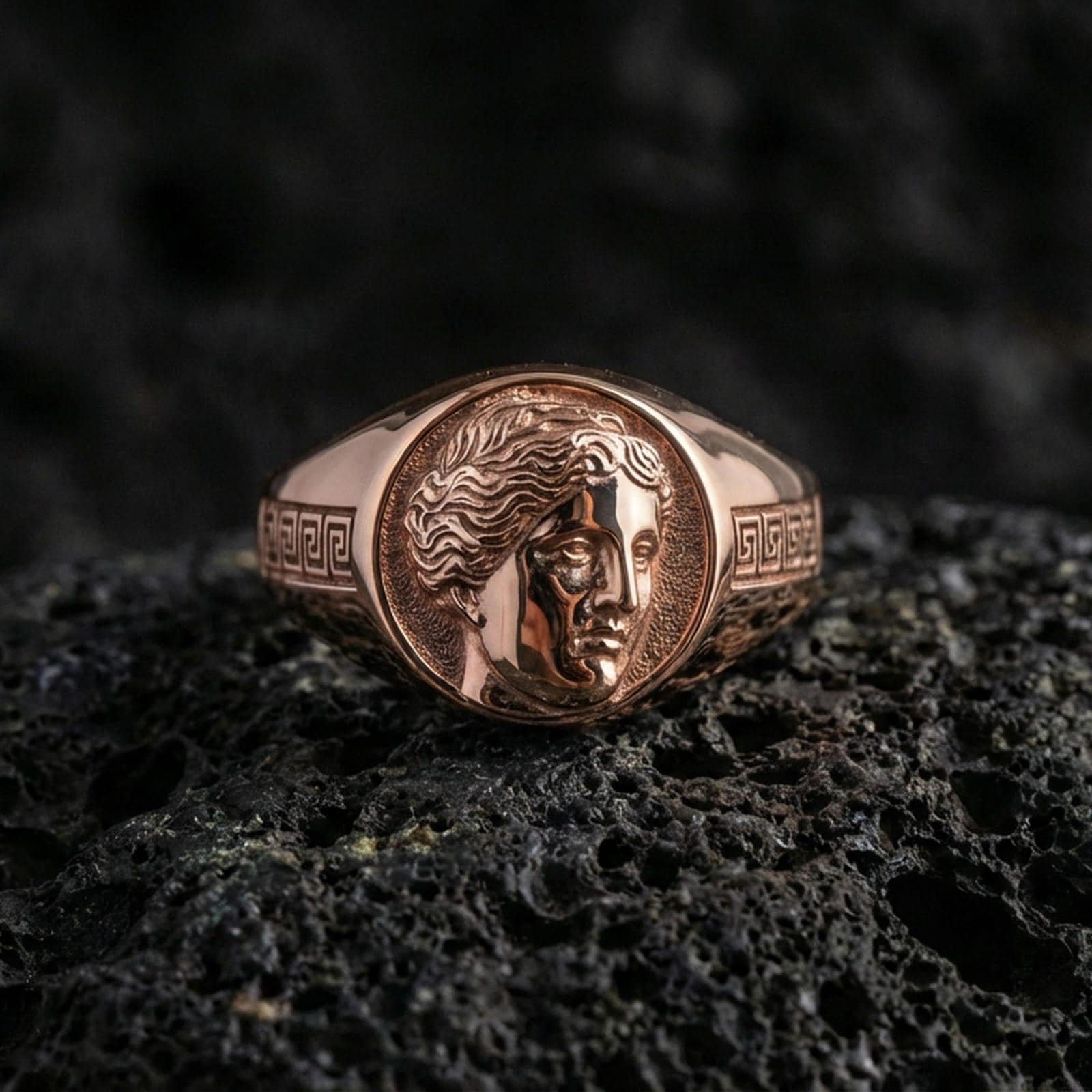 Silver Venus ring in a rose gold plated finish on volcanic rock, feminine goddess profile engraving with classical Greek pattern, dark studio close-up