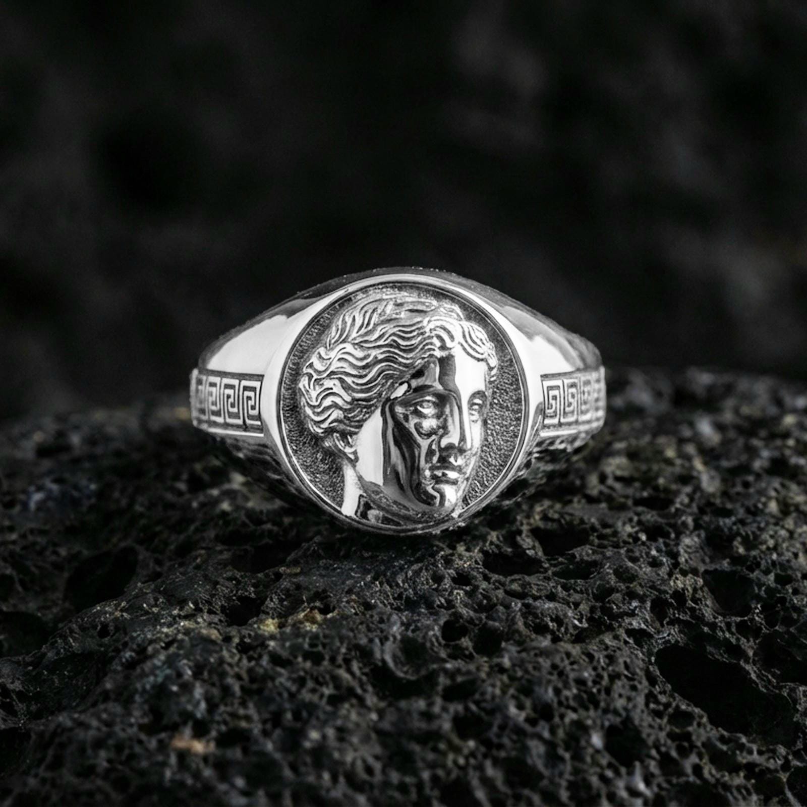 Roman Venus portrait ring in polished silver finish on volcanic rock, classic coin-style face engraving with meander border, premium studio close-up