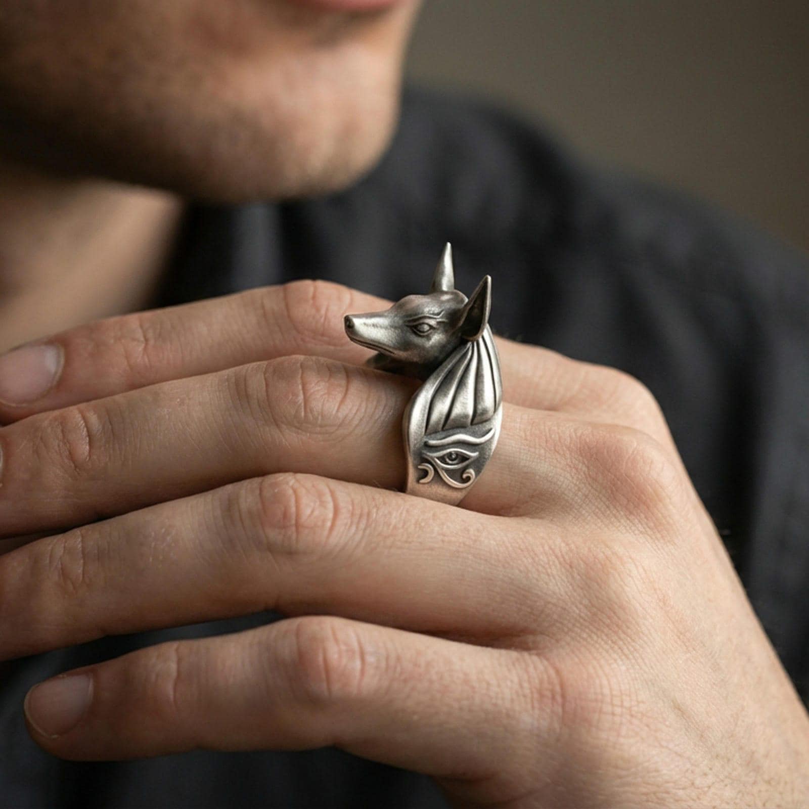 Sterling silver Anubis ring in an oxidized finish worn on finger, jackal head silhouette and Eye of Horus engraving visible, lifestyle hand close-up