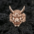 Load image into Gallery viewer, Sterling silver oni ring in a rose gold plated finish on volcanic rock, yokai demon mask design with sculpted horns and fangs, high-end close-up
