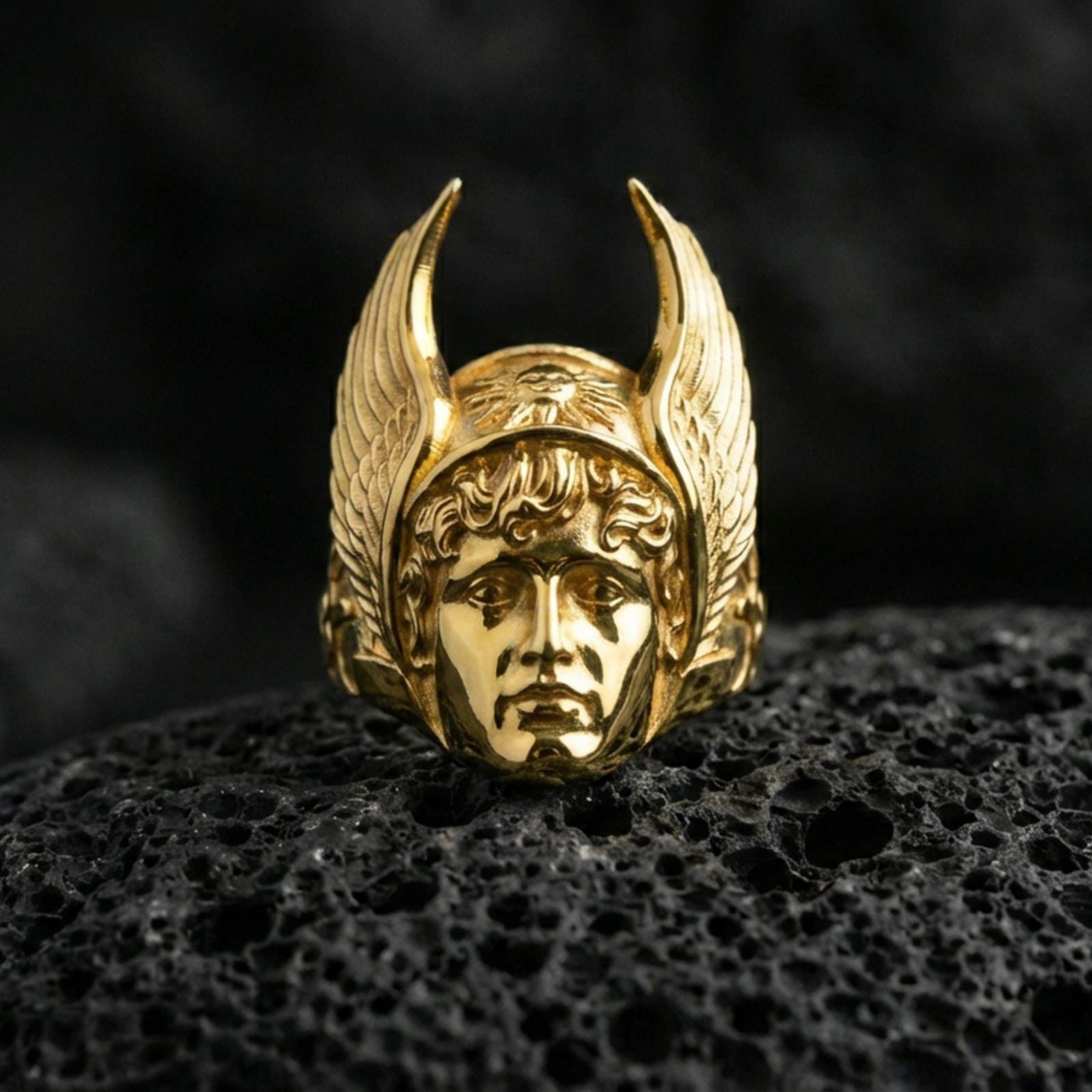 Greek Hermes ring in a gold plated finish on volcanic rock, winged helmet and classic deity face carving, luxury macro product photo