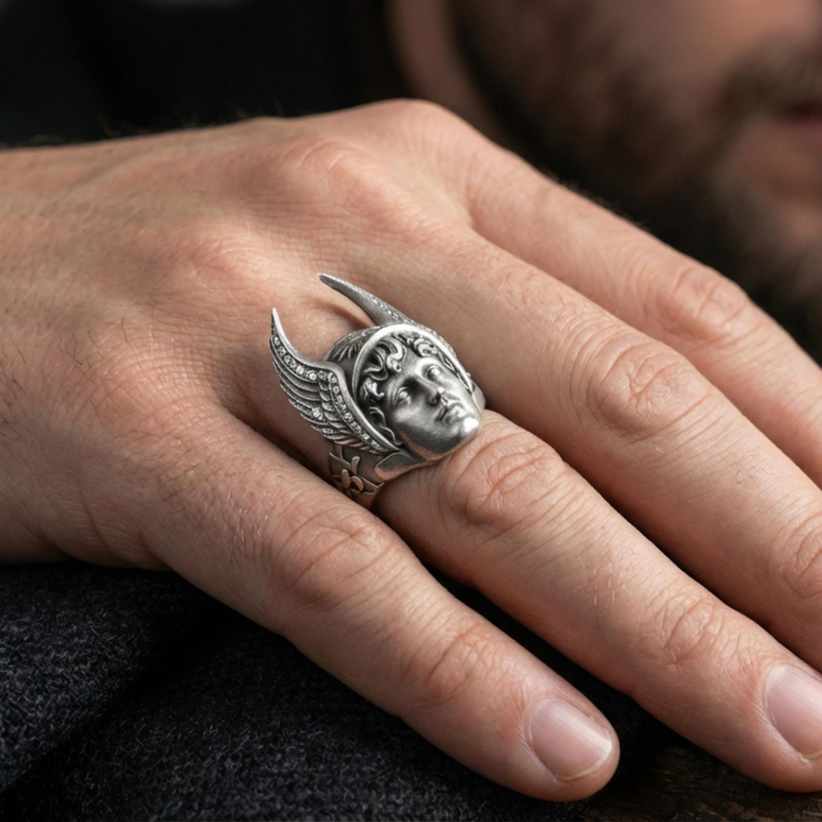 Sterling silver Hermes ring in an oxidized finish worn on finger, Greek god winged helmet face visible, dark aesthetic lifestyle close-up