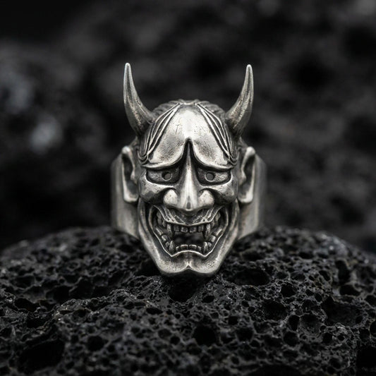 Sterling silver Hannya mask ring in an oxidized finish on volcanic rock, Japanese demon face with horns and grim expression, macro studio shot