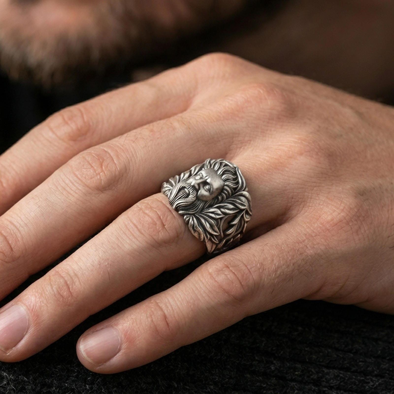 Oxidized silver ring worn on finger, bold bearded face and laurel leaf design, natural lifestyle hand shot with crisp focus
