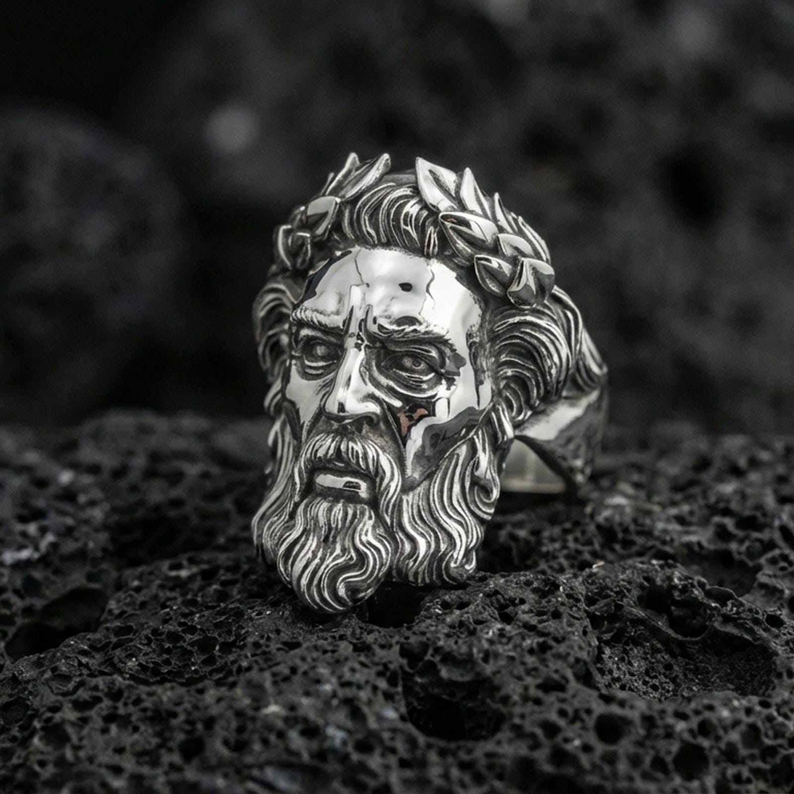 Polished silver Zeus ring featuring classical Greek god portrait and laurel wreath relief, centered close-up on dark volcanic stone
