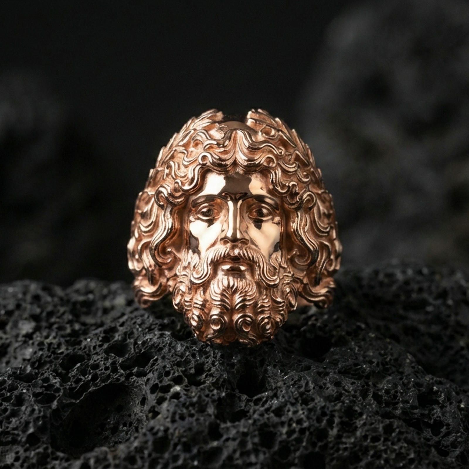 Rose gold plated Zeus head ring with sculpted mythology face and ornate hair texture, sharp close-up product photography on volcanic rock