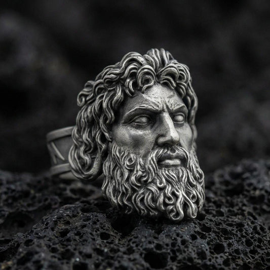 Detailed Zeus signet ring crafted in oxidized sterling silver, intense Greek god facial expression, macro product shot on textured volcanic rock background