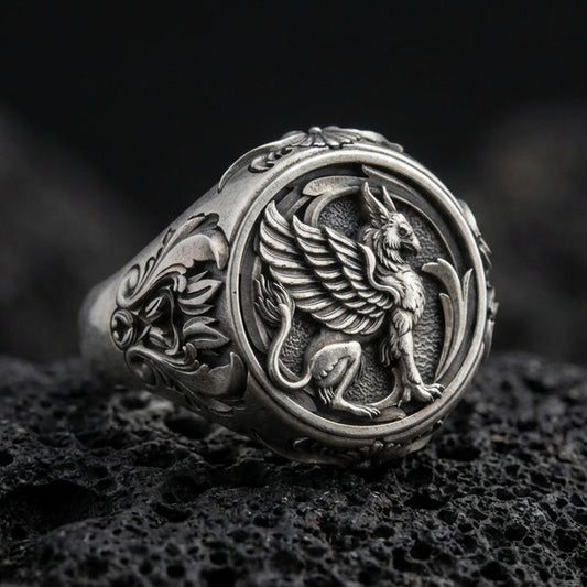 Detailed griffon ring crafted in oxidized sterling silver, winged mythical creature relief, macro product shot on textured volcanic rock background