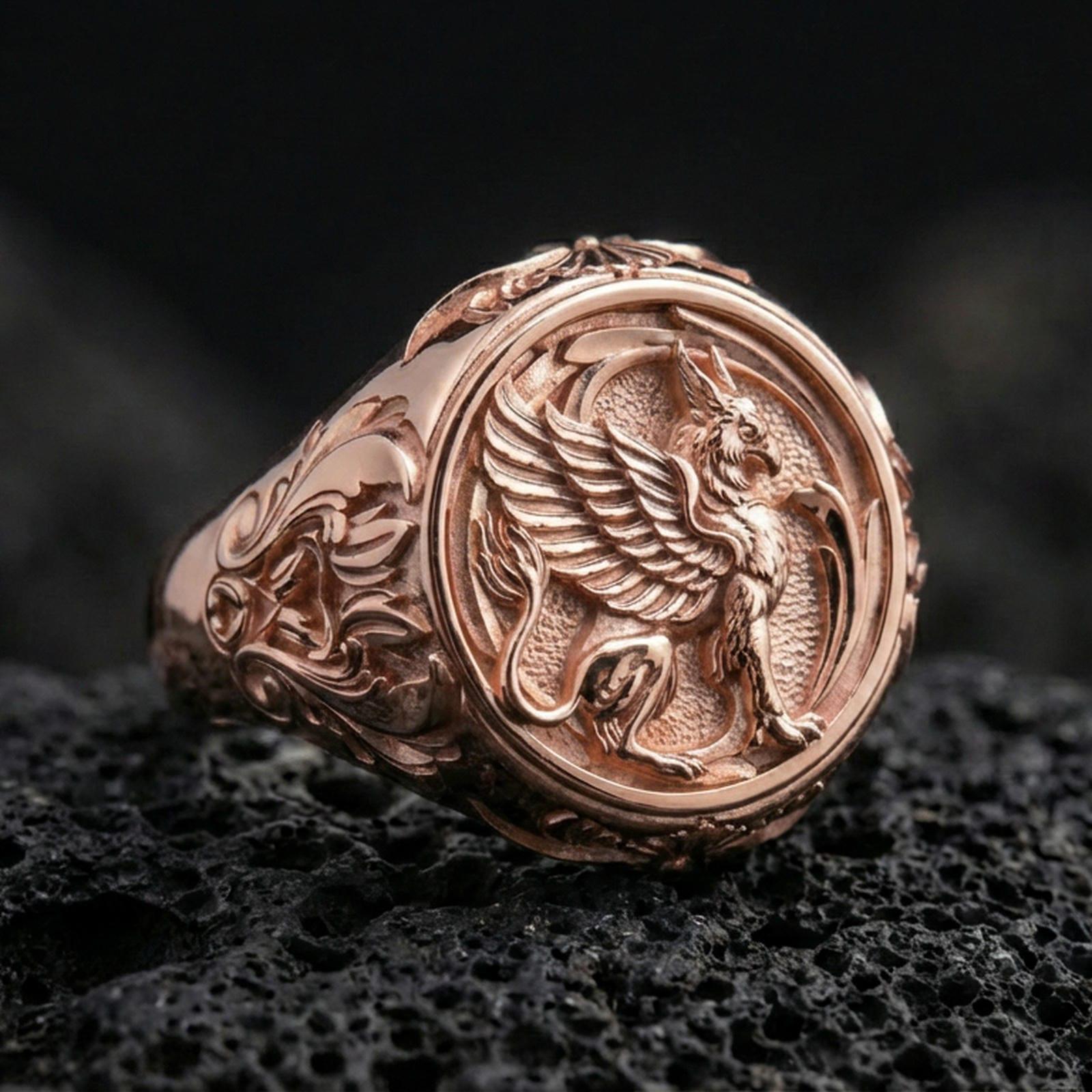 Rose gold plated griffon ring showcasing detailed winged beast engraving and refined sculptural texture, sharp close-up on volcanic rock