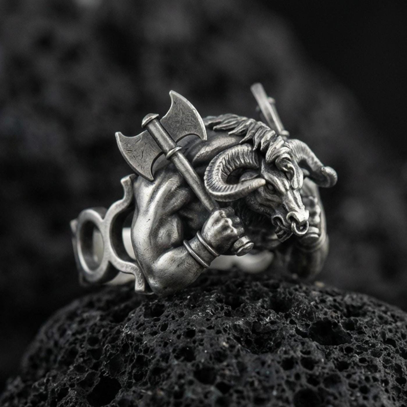 Detailed Minotaur ring crafted in oxidized sterling silver, muscular bull-headed beast holding double axe, macro product shot on textured volcanic rock background